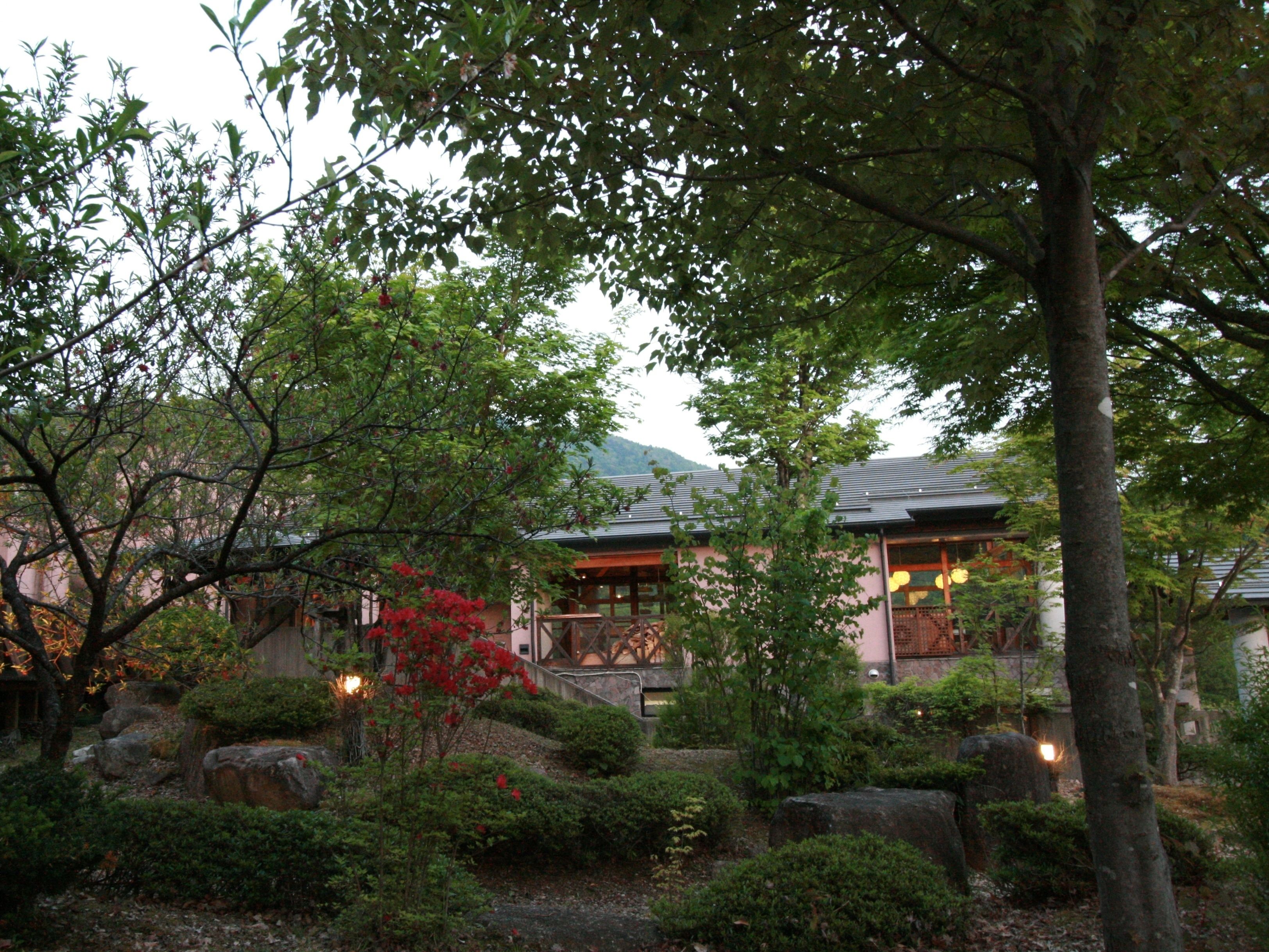 A traditional Japanese-style building with a wooden exterior and a sloped roof, surrounded by lush greenery and rocks.