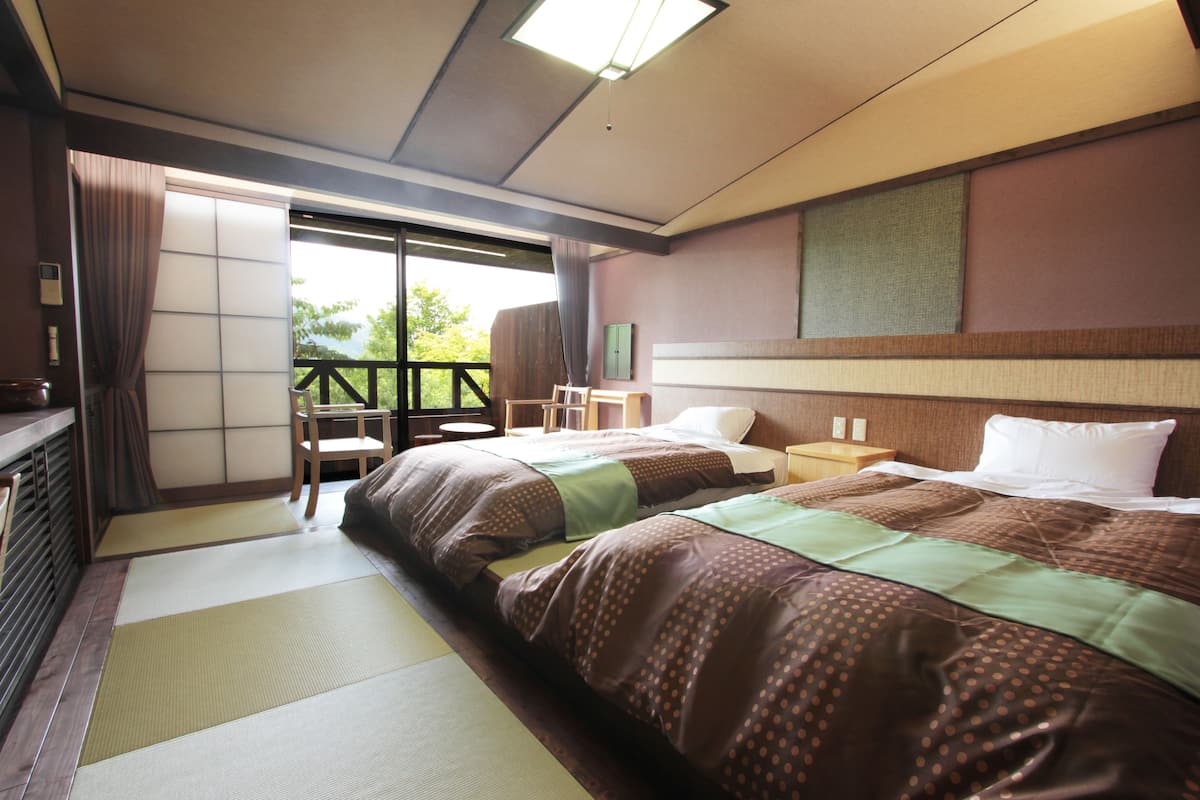 A hotel room with a large bed, a wooden nightstand, a chair, and a view of the outdoors through a sliding door.