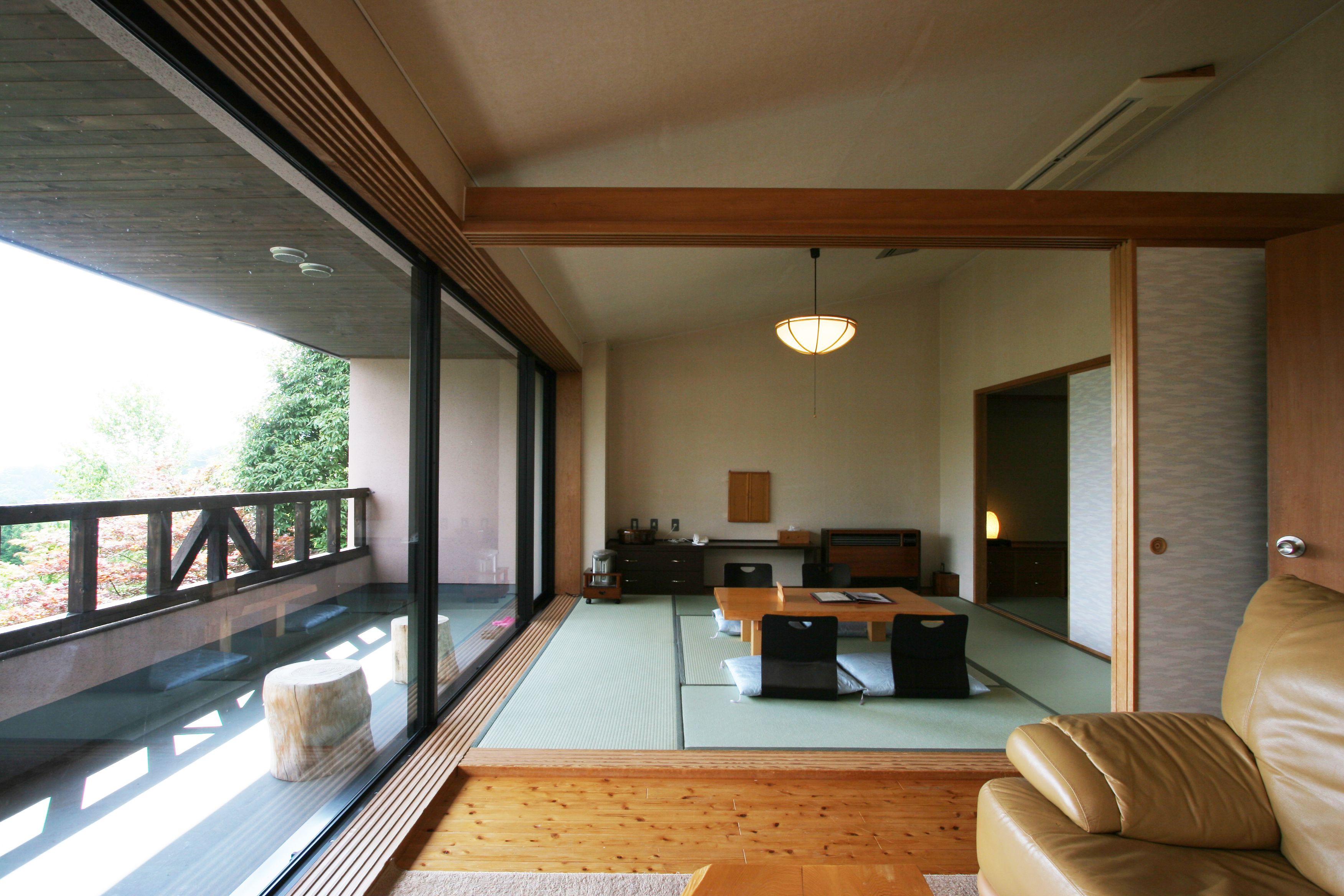 Un interno moderno con pavimento in legno, sedute in tatami, un divano in pelle e un'area pranzo con tavolo e sedie.