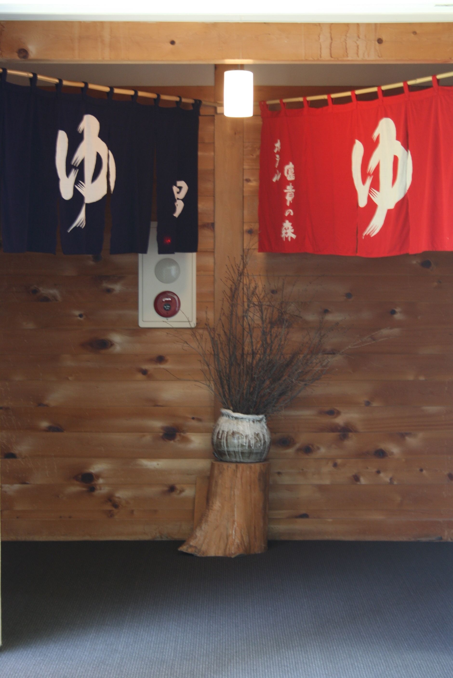Een houten wand met twee Japanse vlaggen, een klein houten kastje en een vaas met takken.