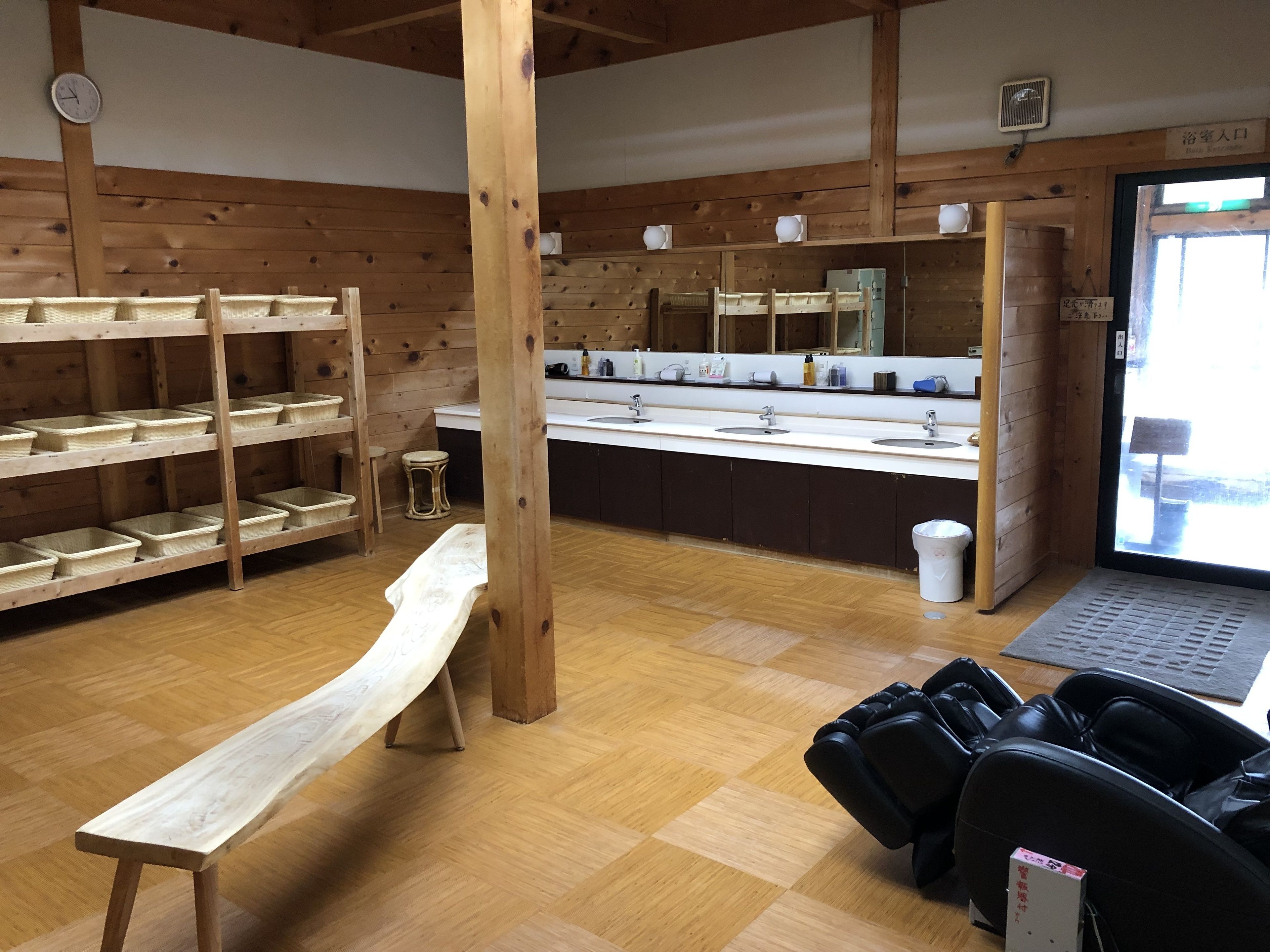 A wooden interior with a long bench, a row of sinks, and shelves with baskets.