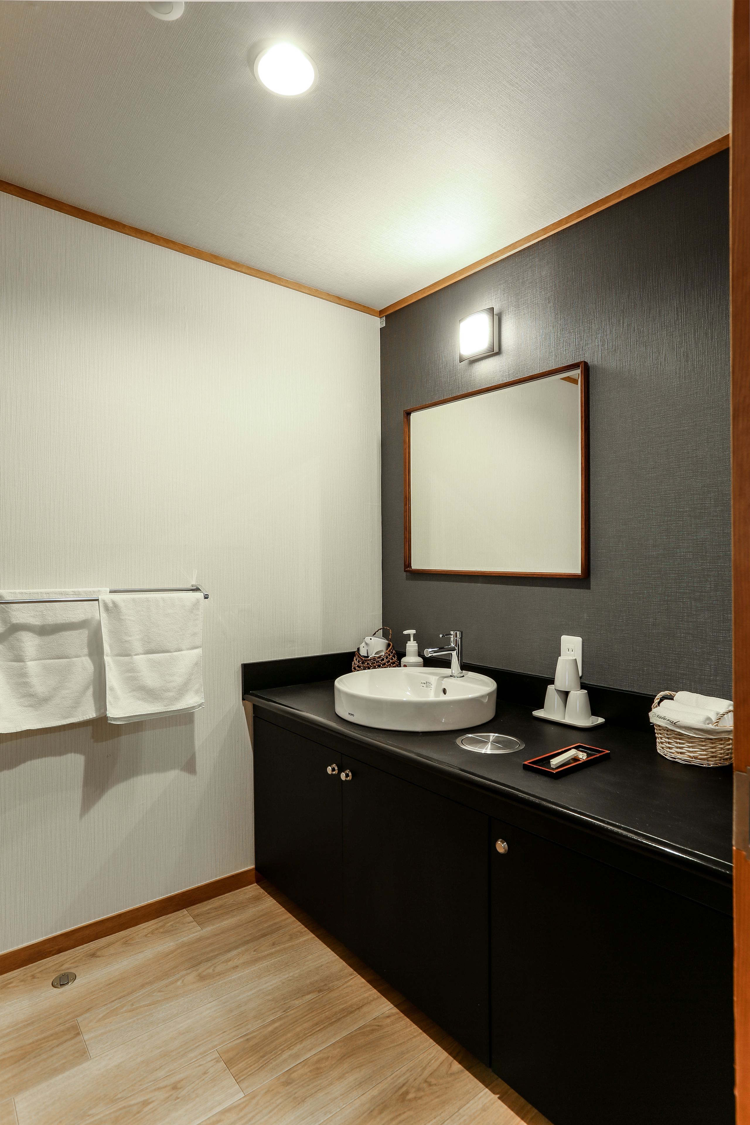 A bathroom with a white sink, a mirror, and a wooden floor.
