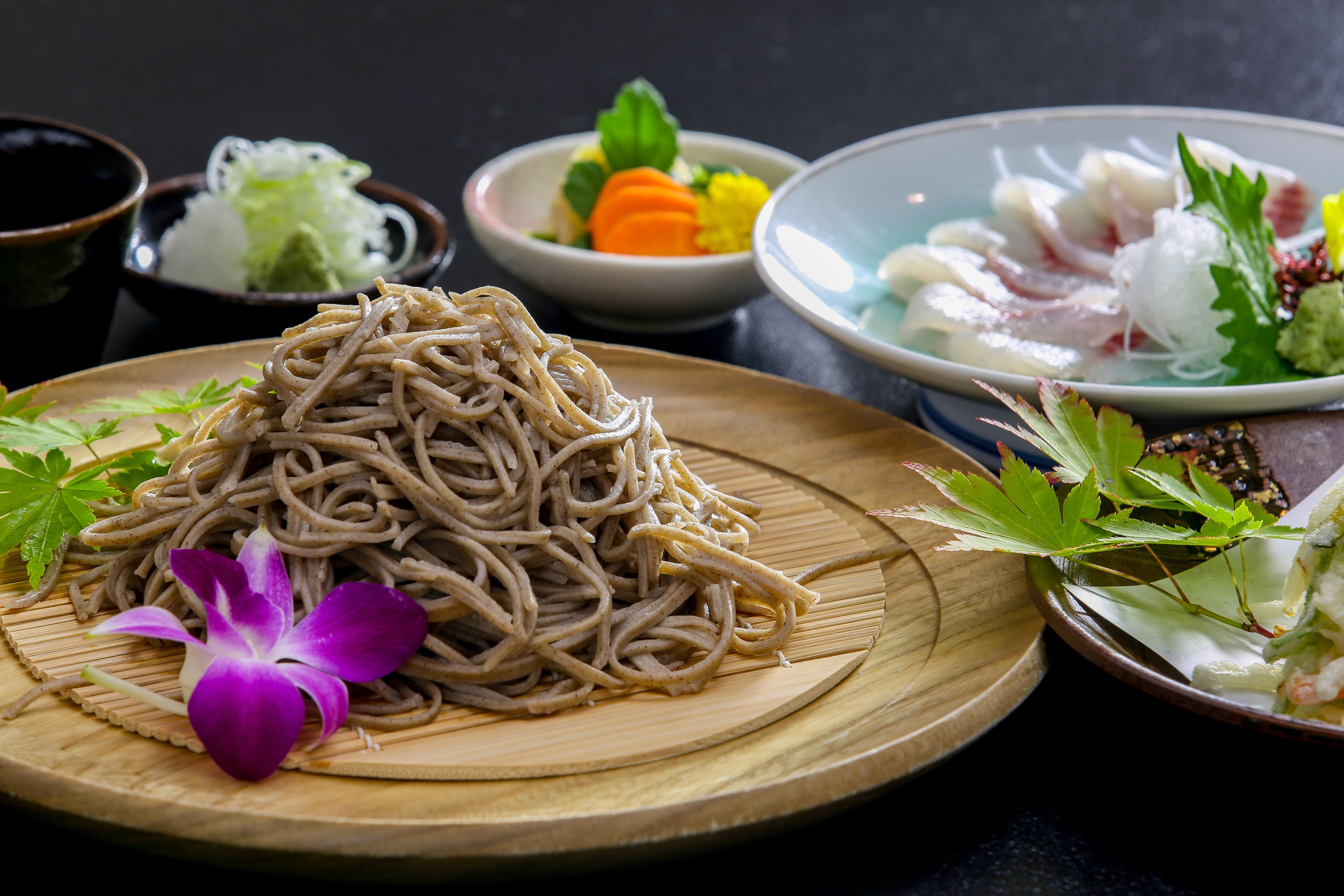 A variety of dishes including noodles, sashimi, and vegetables on a wooden table.