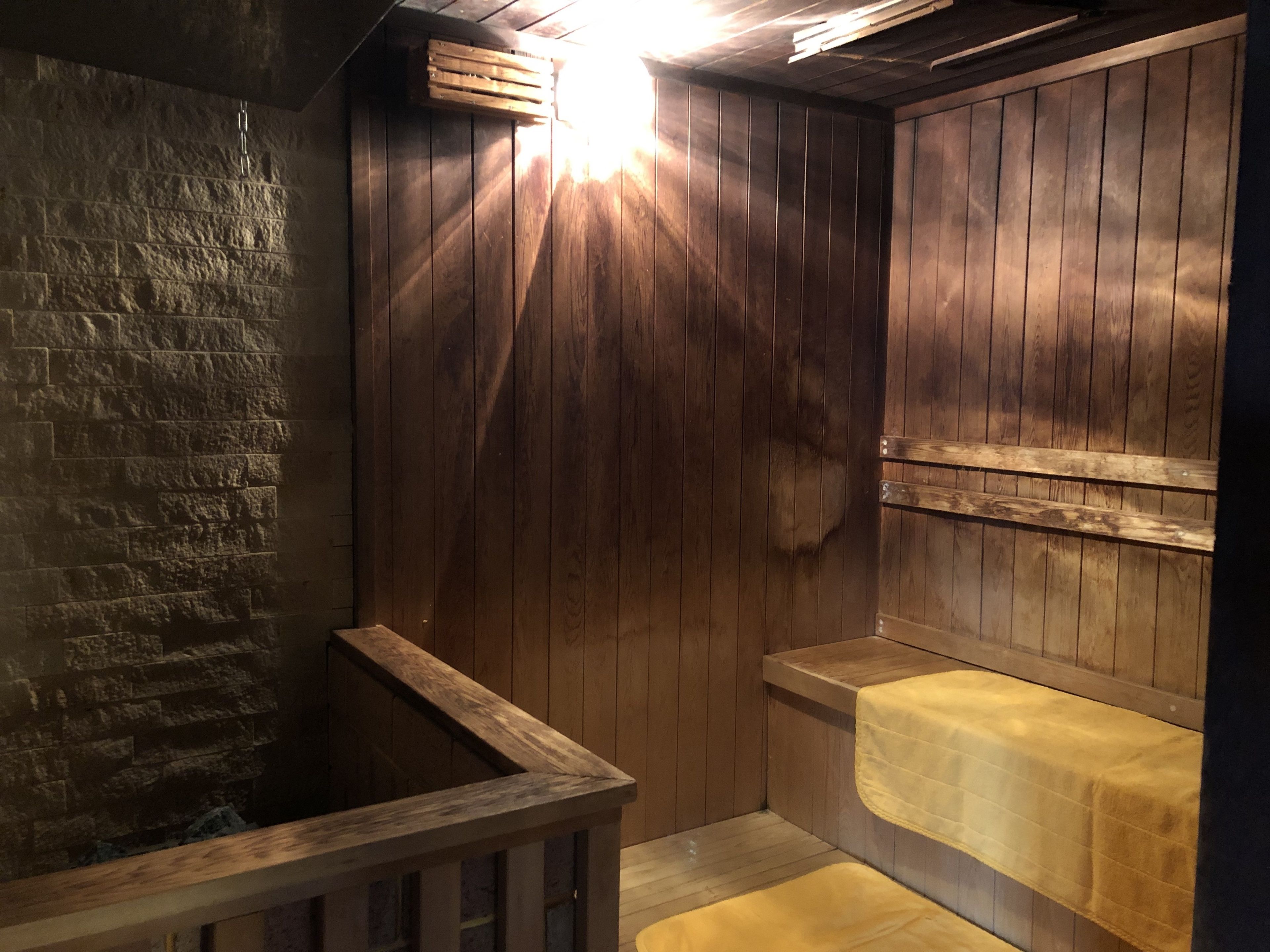 Una sauna de madera con pared de piedra, bancos de madera y un banco con toalla.