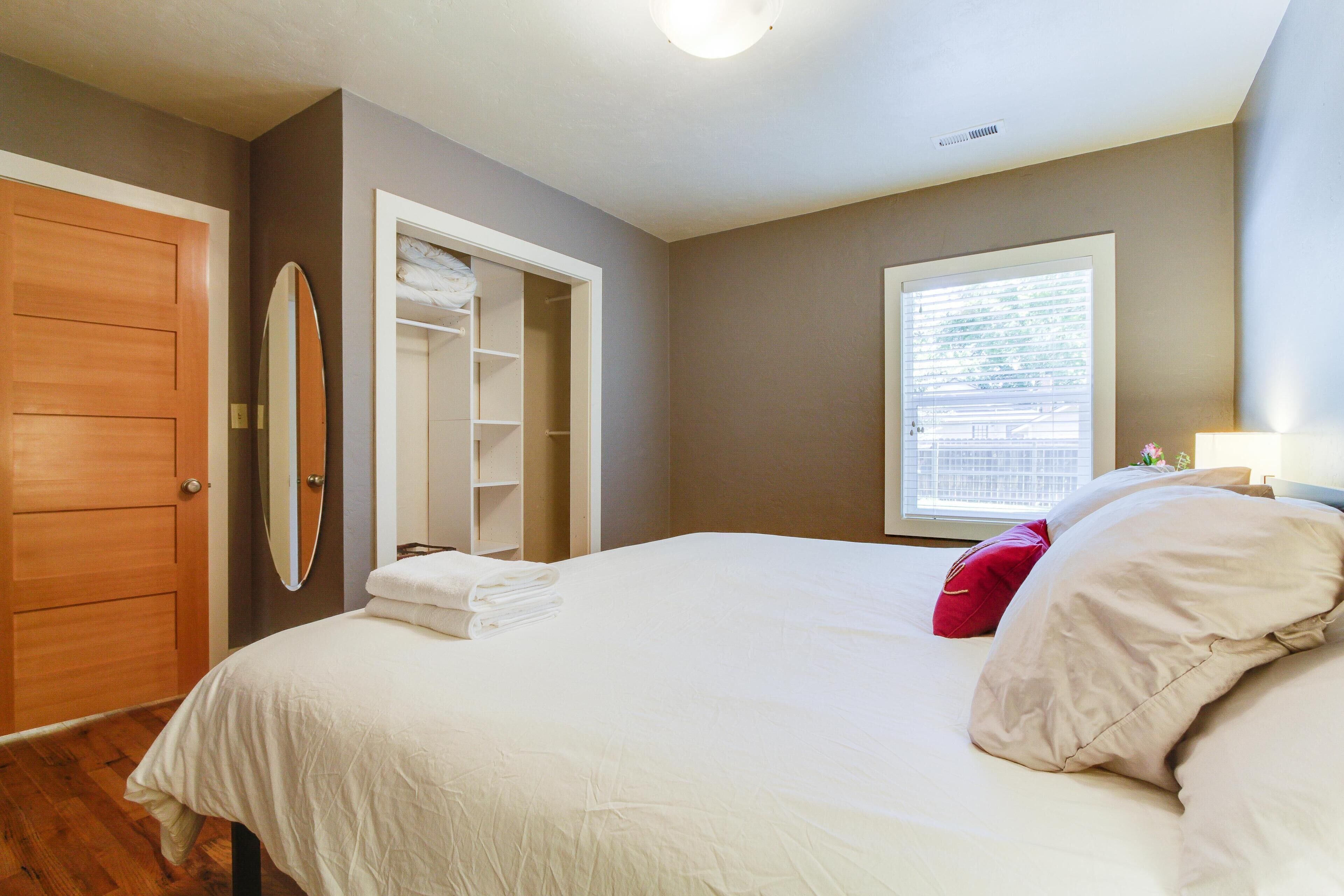 A bedroom with a bed, a closet, a window, and a mirror.