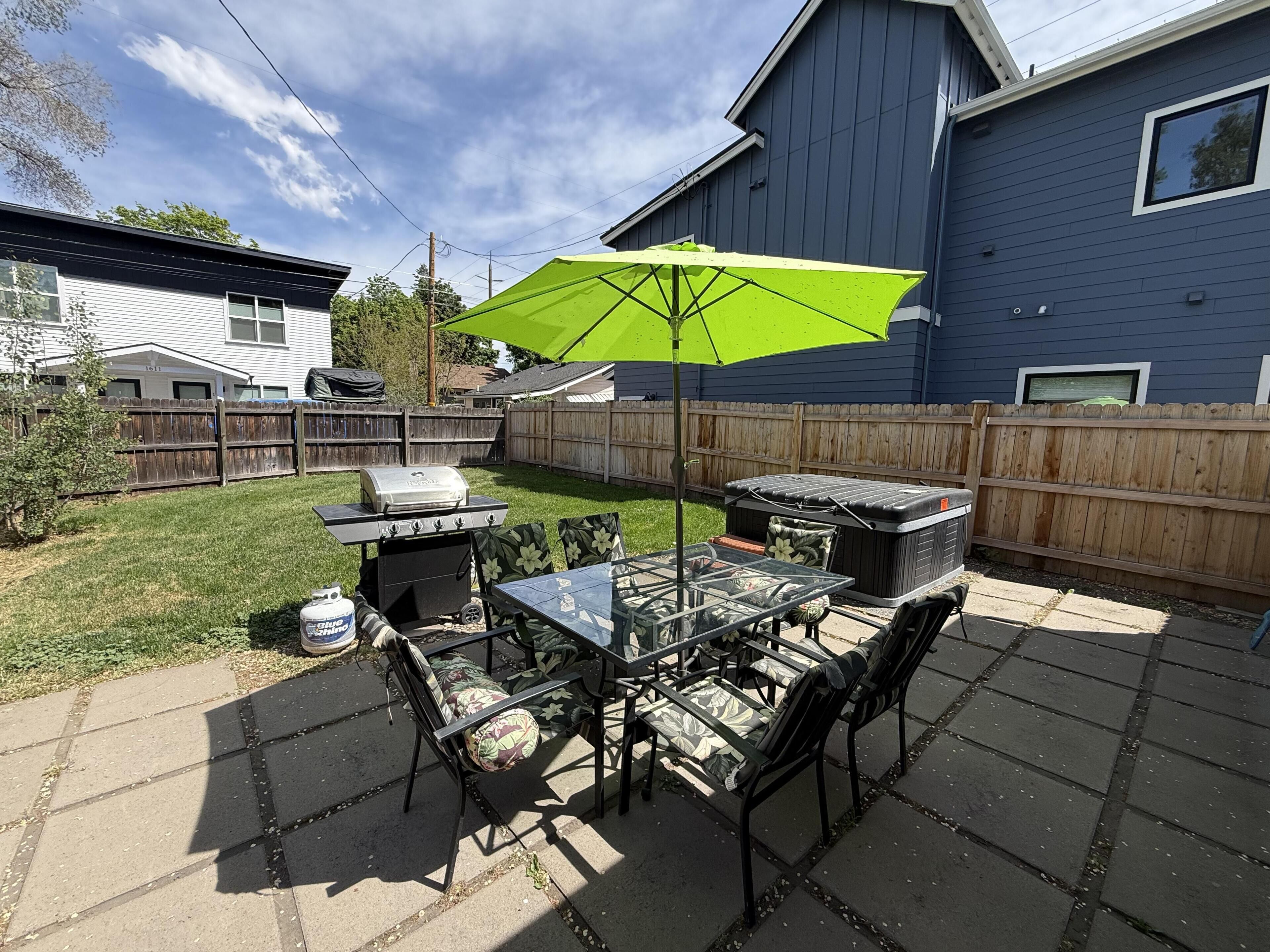 A backyard patio with a table, chairs, a grill, and a green umbrella.