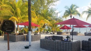 A beach area with wicker furniture, red umbrellas, and a sign indicating a VIP area. - Experience Luxury on the Island of Isla Mujeres  (ISLA MUJERES)