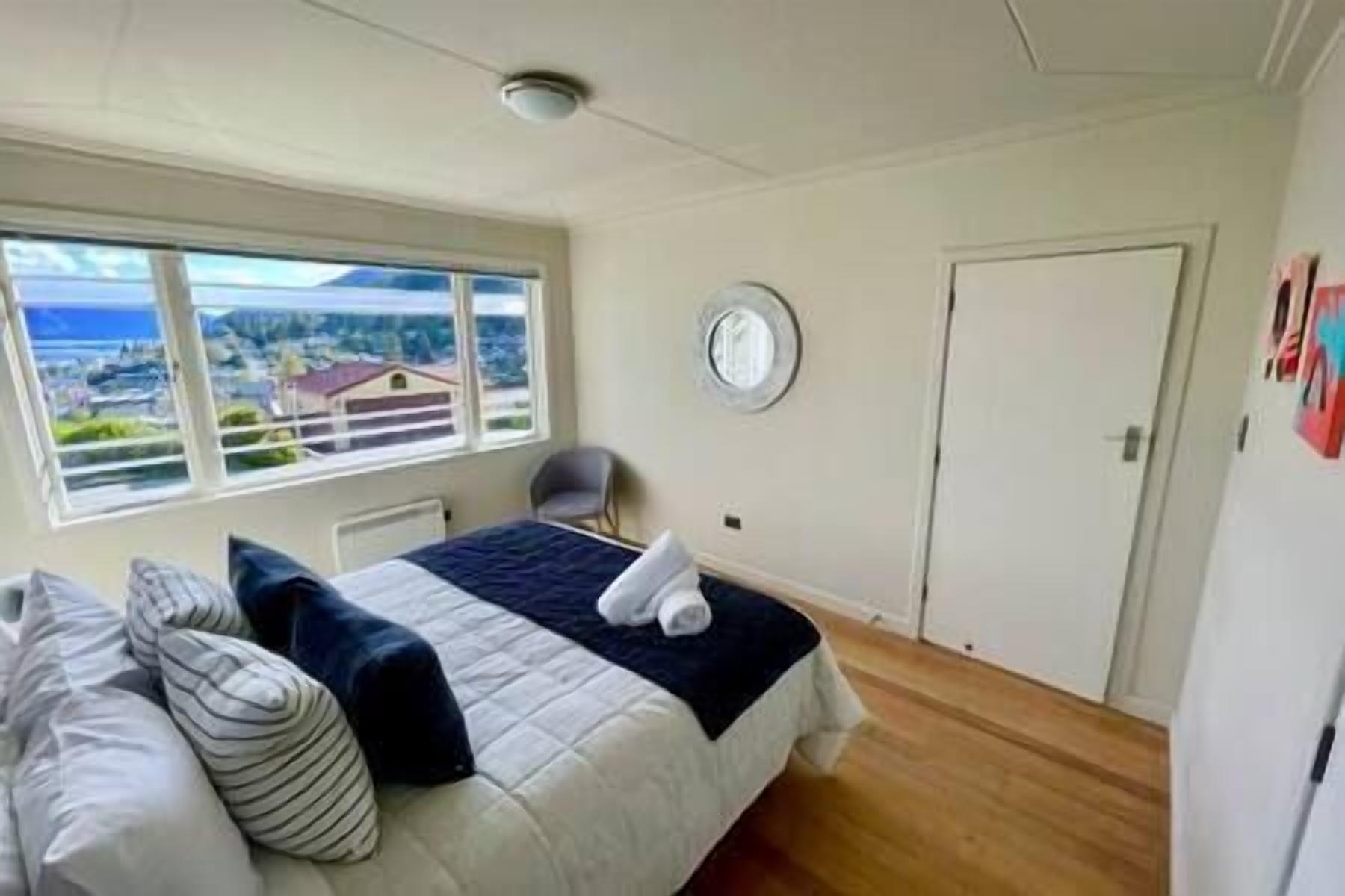 A bedroom with a bed, a chair, a window with a view, a door, and a wall-mounted clock.