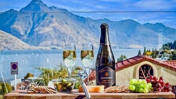 Una mesa con una botella de vino, copas, uvas y un cuenco de aceitunas.