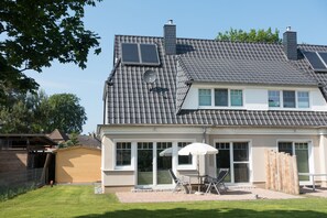 Et toetagers hus med et tegltag, en overdækket terrasse med udendørs møbler og en hegnet baghave.
