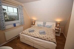 Un dormitorio con cama, mesitas de noche, lámparas, una ventana con cortinas y un radiador.