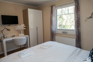 A hotel room with a bed, a desk with a chair, a television mounted on the wall, and a window with curtains.