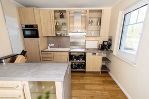 Una cocina moderna con armarios de madera, horno empotrado, lavavajillas y ventana que proporciona luz natural.