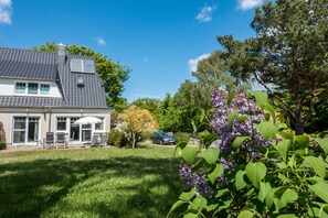 A house with a patio, a car, and a tree with purple flowers.