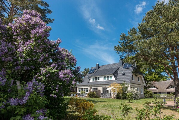 A two-story house with a sloped roof, solar panels, and a well-maintained garden with purple flowers.