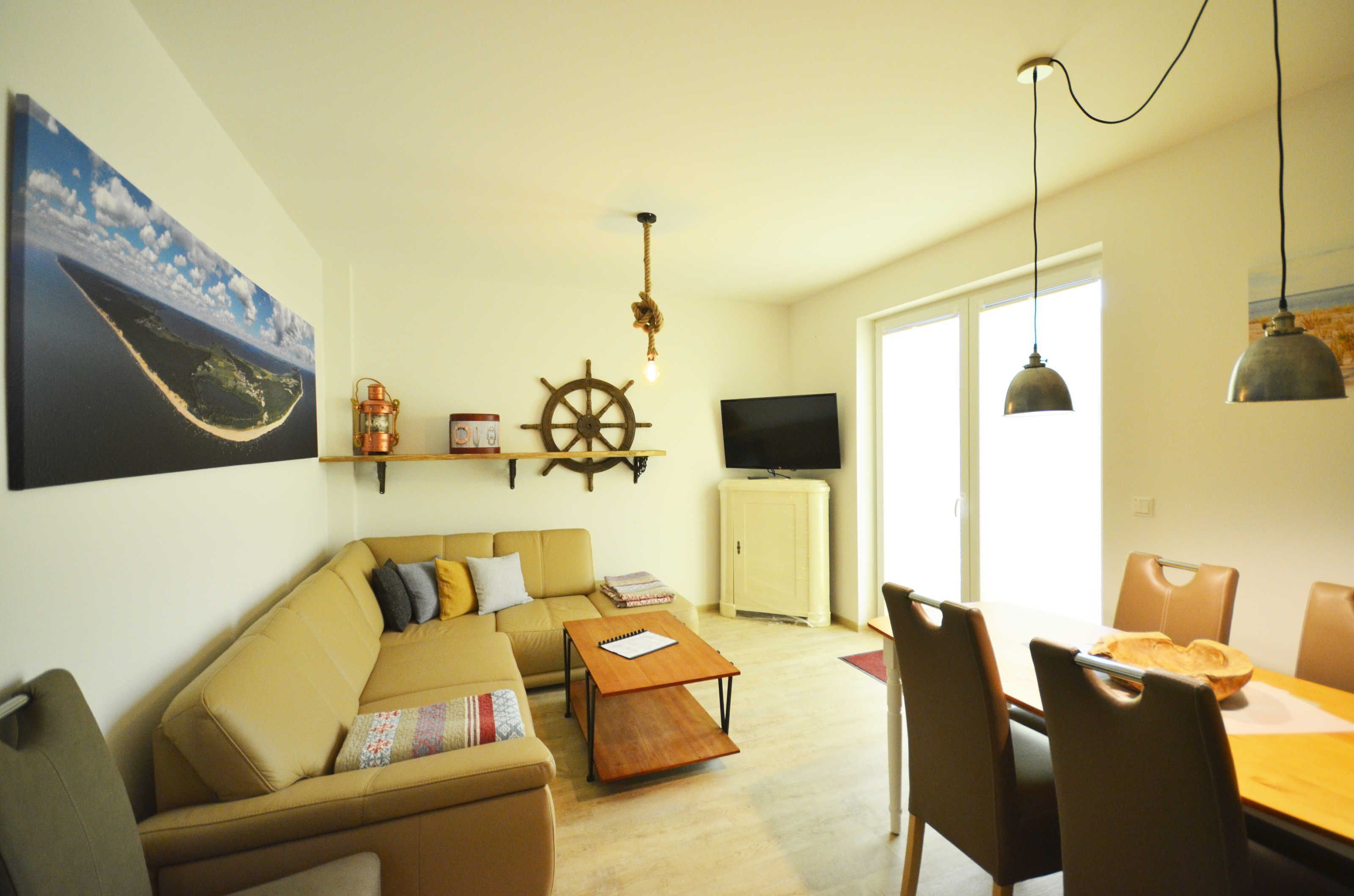 Una sala de estar con sofá, mesa de centro, mesa de comedor con sillas, televisor y un adorno de timón de barco.