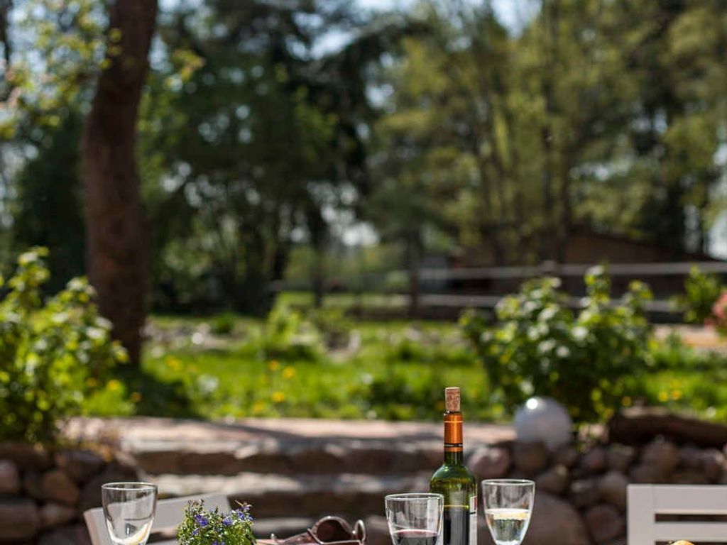 Une table dressée à l’extérieur, avec une bouteille et des verres, entourée de verdure et d’un mur de pierres.