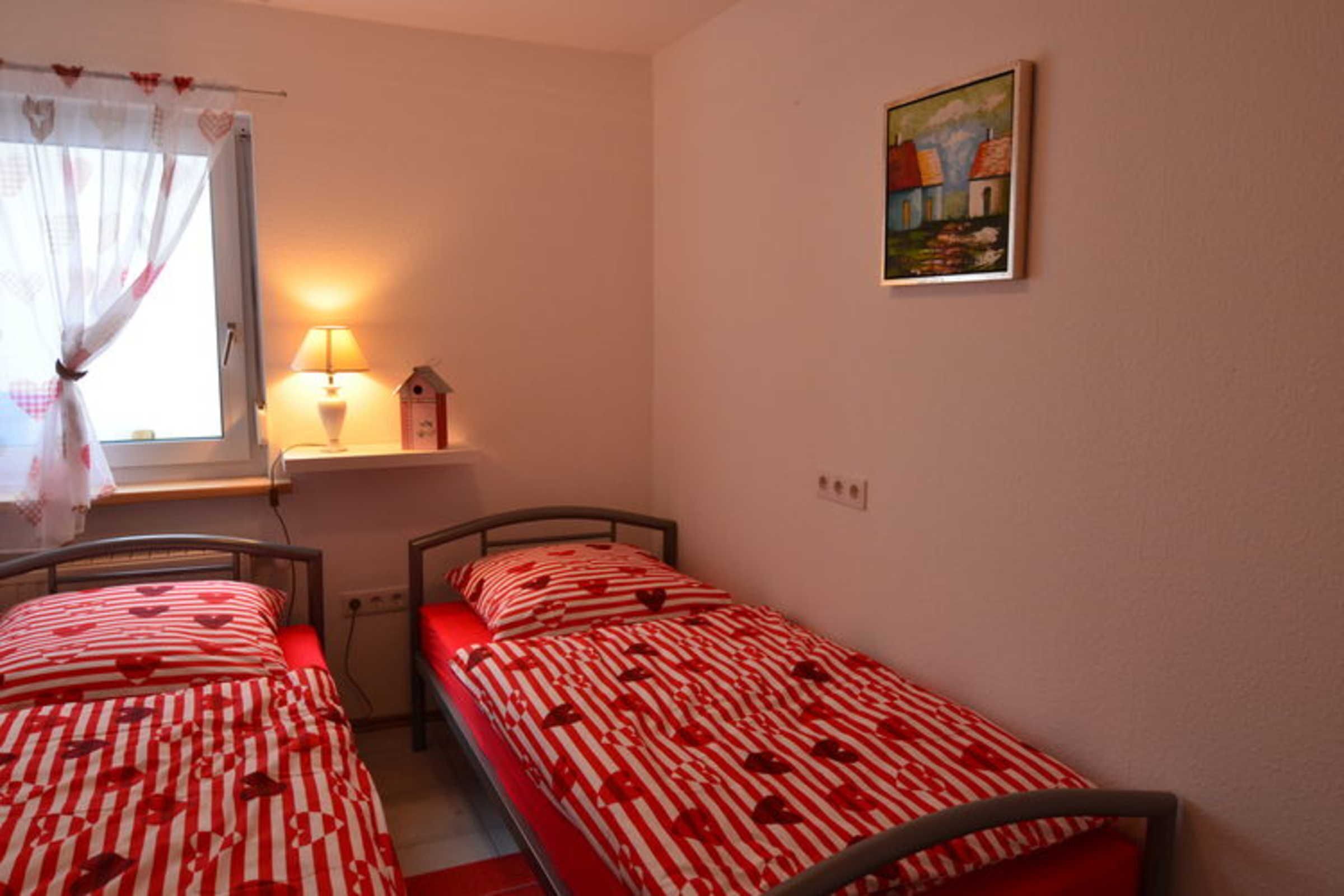 A bedroom with two single beds, a window with curtains, a bedside lamp, and a wall-mounted painting.