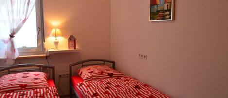 A bedroom with two single beds, a window with curtains, a bedside lamp, and a wall-mounted painting.