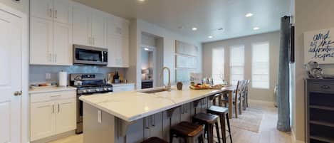 A spacious kitchen with white cabinets, a central island with stools, a microwave, and a stove.
