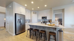 A modern kitchen with white cabinets, stainless steel appliances, a central island with stools, and a built-in microwave. - Endless Adventures-Pool is Open! (Washington)