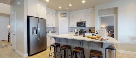 A modern kitchen with white cabinets, stainless steel appliances, a central island with stools, and a built-in microwave.