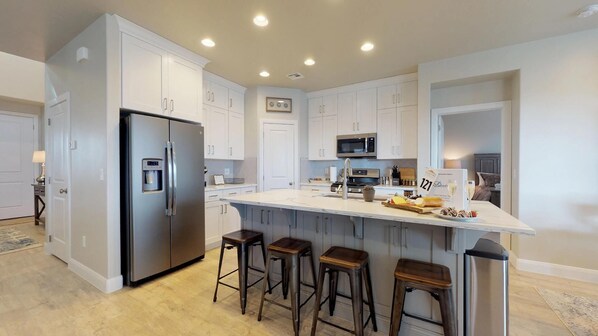 A modern kitchen with white cabinets, stainless steel appliances, a central island with stools, and a built-in microwave.
