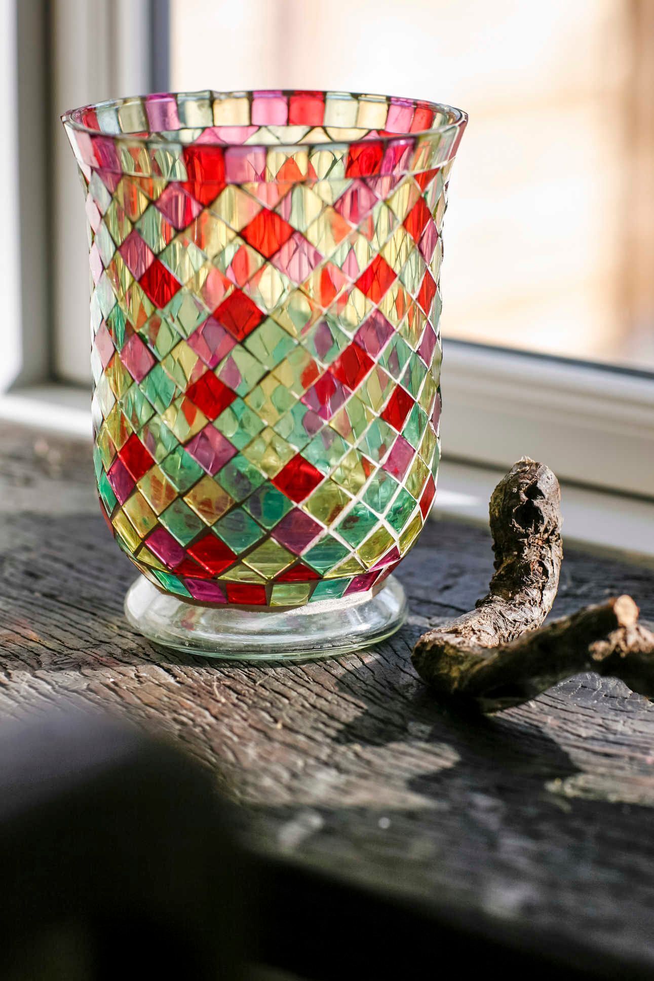 Eine farbenfrohe Glas-Mosakschale auf einer Holzoberfläche nahe eines Fensters.