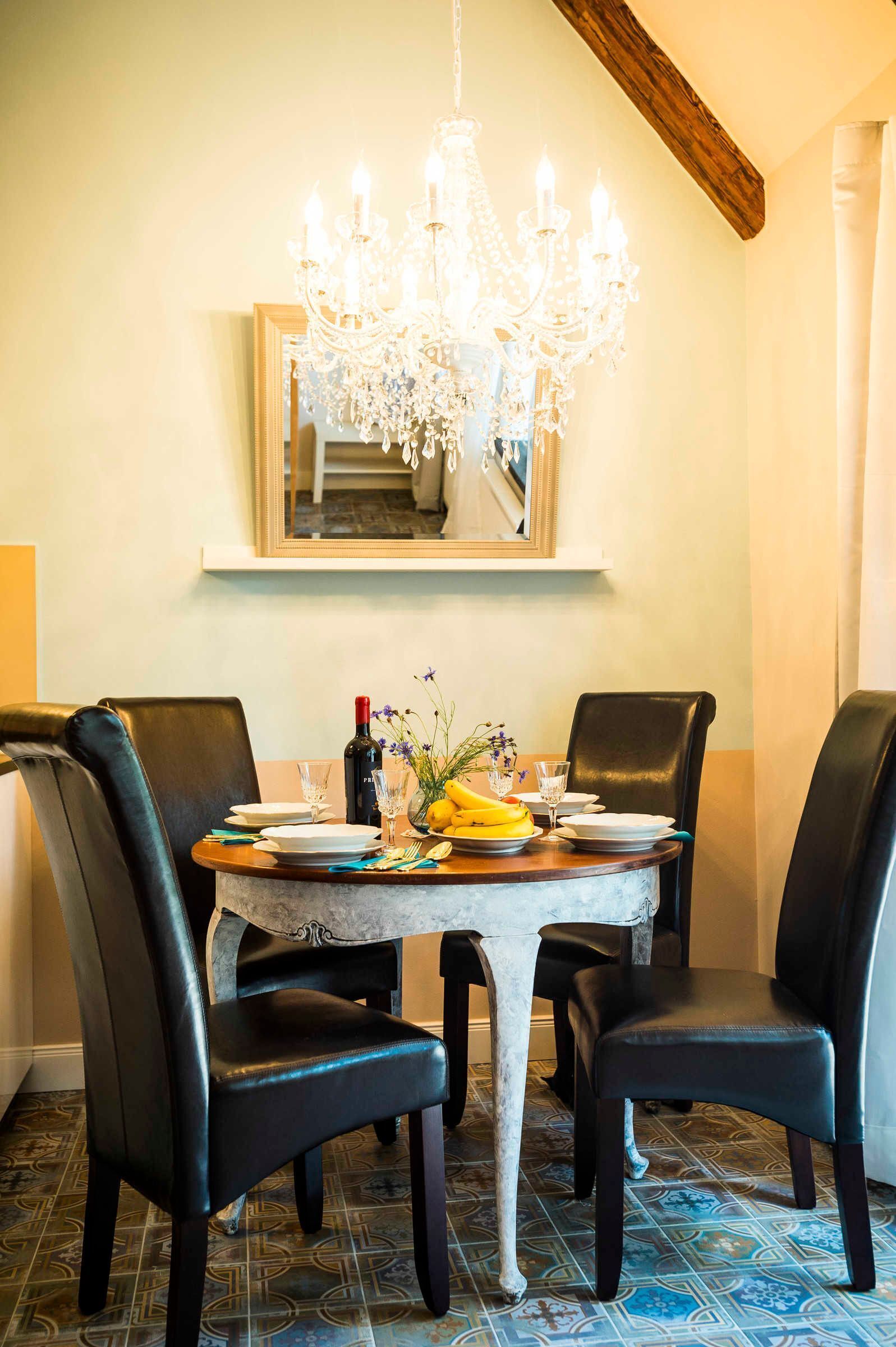 Un coin repas agrémenté d’un lustre, d’une table dressée pour quatre personnes et d’un miroir placé au-dessus de la table.