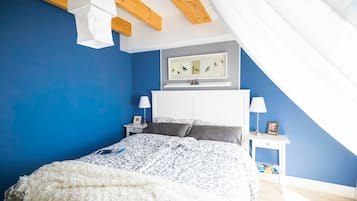 A bedroom with a bed, a nightstand, a lamp, a framed picture on the wall, and a ceiling with wooden beams.