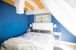 Et soveværelse med en seng, et natbord, en lampe, et billede i ramme på væggen og et loft med træbjælker.