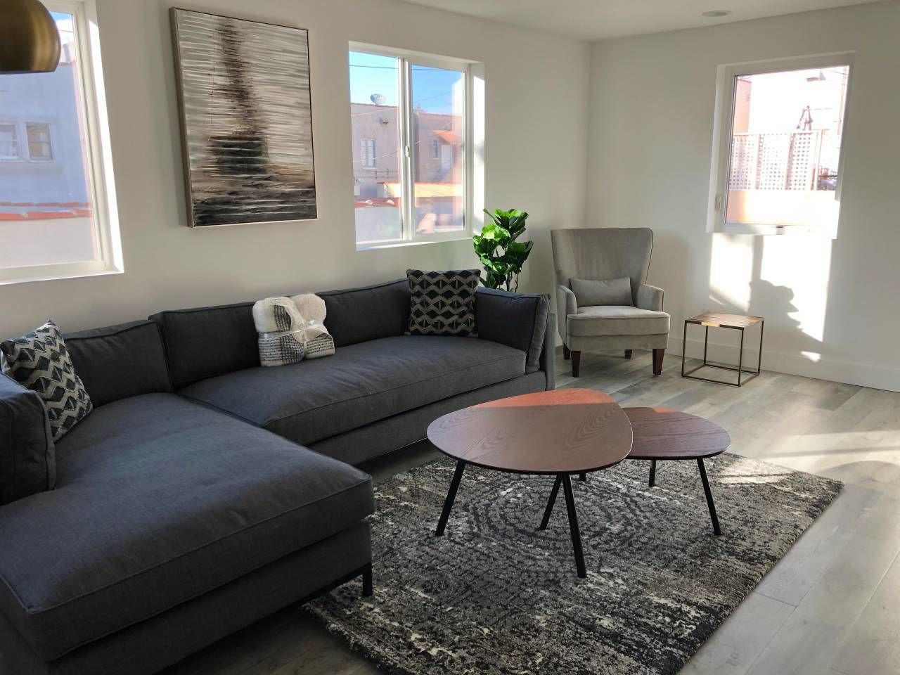 A modern living room with a grey sectional sofa, two round coffee tables, a grey armchair, and a large window providing natural light.