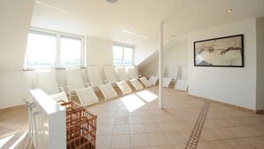 A spacious waiting area with multiple white chairs arranged in rows, large windows allowing natural light, and a framed artwork on the wall. - Double room - Hotel Poinger Hof (Poing)