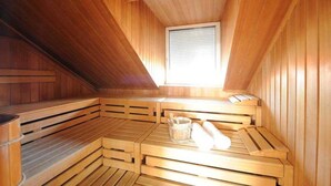 A sauna with wooden benches arranged in a semi-circular pattern, a window at the back, and a wooden bucket with a brush on the floor. - Double room - Hotel Poinger Hof (Poing)