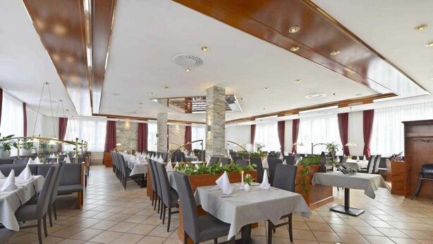 A spacious restaurant with multiple dining tables and chairs, large windows with curtains, and a modern ceiling design. - Double room - Hotel Poinger Hof (Poing)