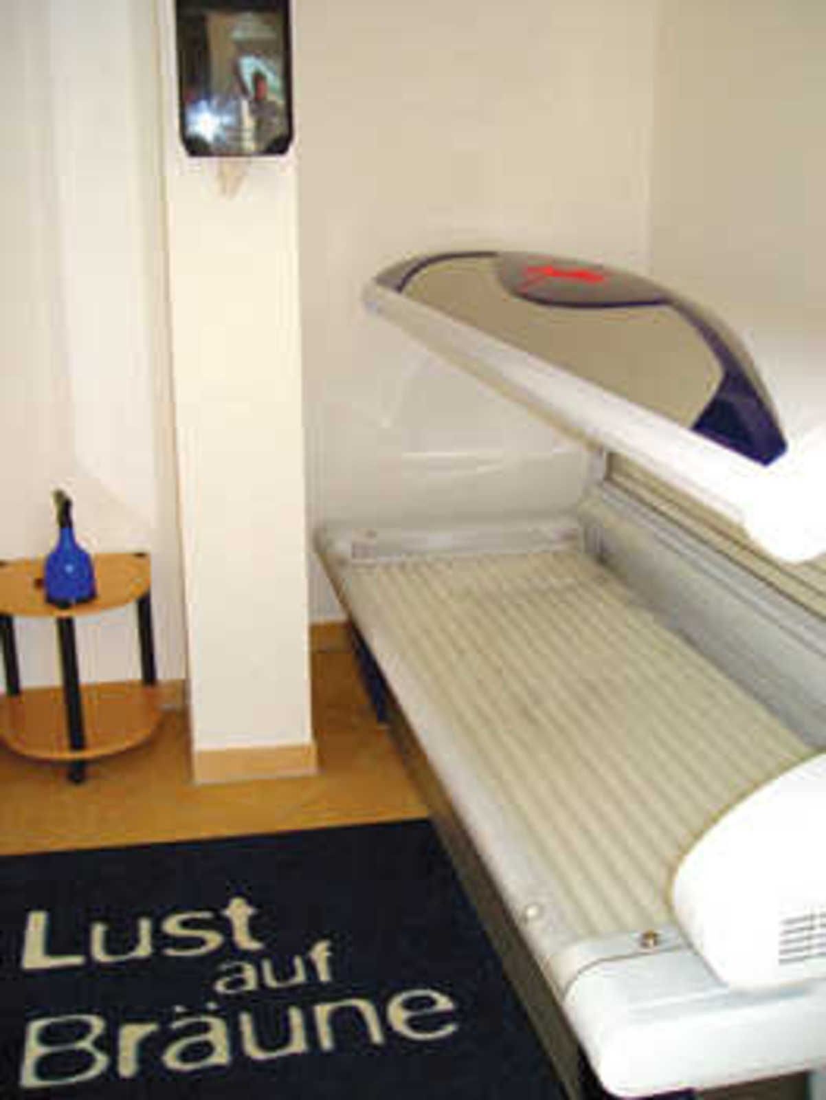 A room with a bed, a small table with a blue object, and a wall-mounted device.