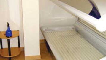 A room with a bed, a small table with a blue object, and a wall-mounted device.
