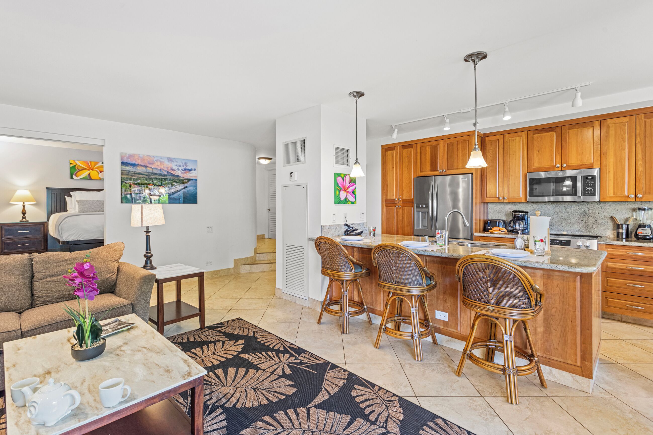 Un apartamento moderno con cocina que cuenta con armarios de madera, un refrigerador de acero inoxidable y un microondas. Hay una zona de comedor con un taburete de bar y una mesa de centro.