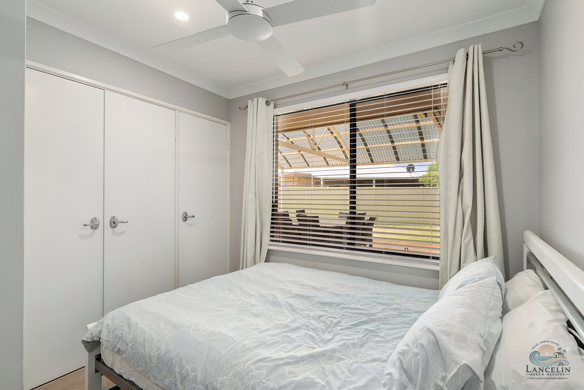 A bedroom with a bed, a ceiling fan, a window with blinds, and a wardrobe.