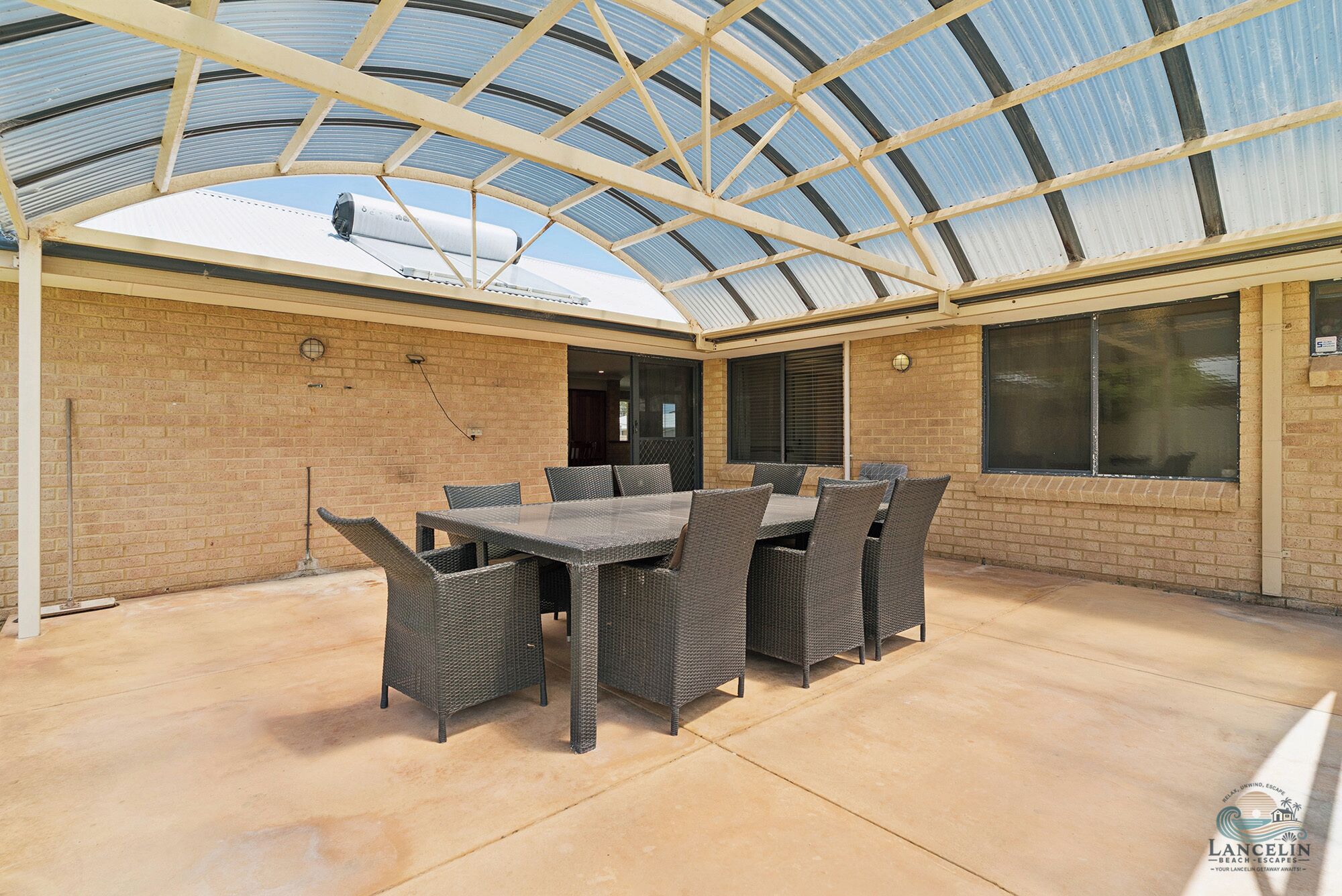 Eine überdachte Terrasse mit Tisch und Stühlen, Backsteinwänden und großen Fenstern.