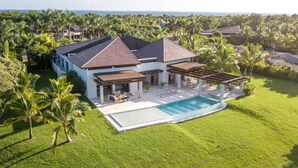 A large house with a swimming pool, surrounded by palm trees and a well-maintained lawn. - Hermosa: Expansive luxury villa w/ pool, Jacuzzi, chef, butler, golf cart (Casa de Campo)