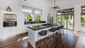 A modern kitchen with a central island, built-in appliances, and large windows. - Hermosa: Expansive luxury villa w/ pool, Jacuzzi, chef, butler, golf cart (Casa de Campo)