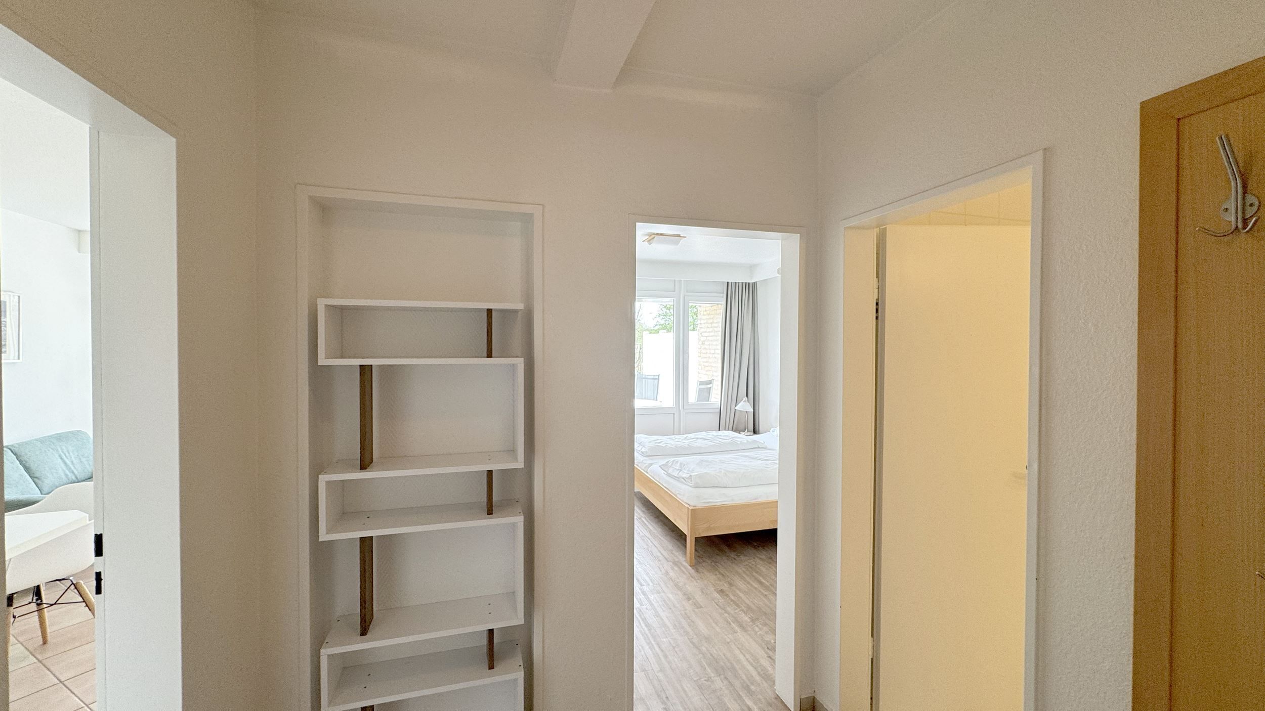 A hallway with a white shelving unit, a bed with a wooden frame, and a door with a metal handle.