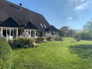Ein Haus mit dunklen Ziegeldach, einer überdachten Veranda mit Stühlen und einem gepflegten Rasen.