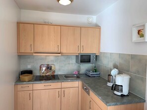 Eine Küche mit Holzschränken, einer Mikrowelle, einem Toaster, einer Kaffeemaschine und einer gefliesten Spritzschutzwand.