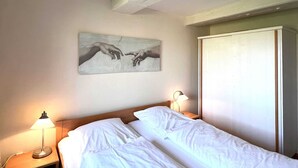 Ett hotellrum med en säng, två sänglampor, en tavla med händer på väggen och en garderob.