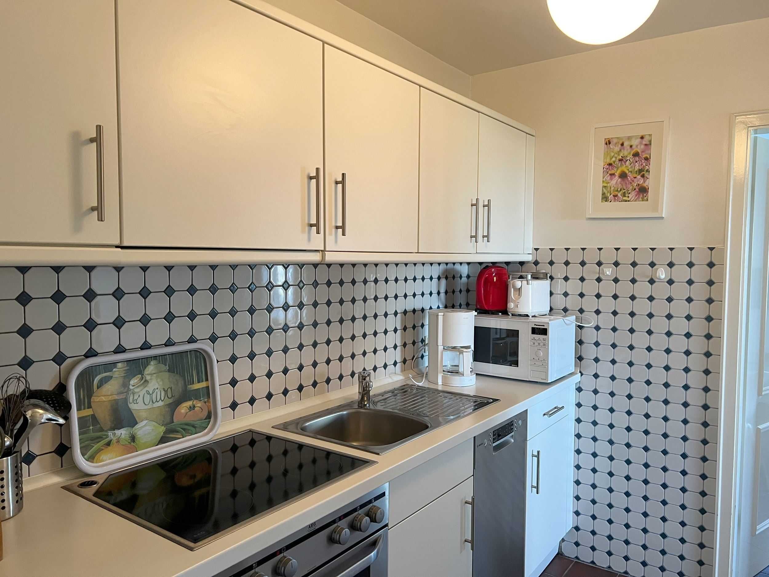 A kitchen with white cabinets, a black and white tiled backsplash, a stove, a microwave, and a coffee maker.