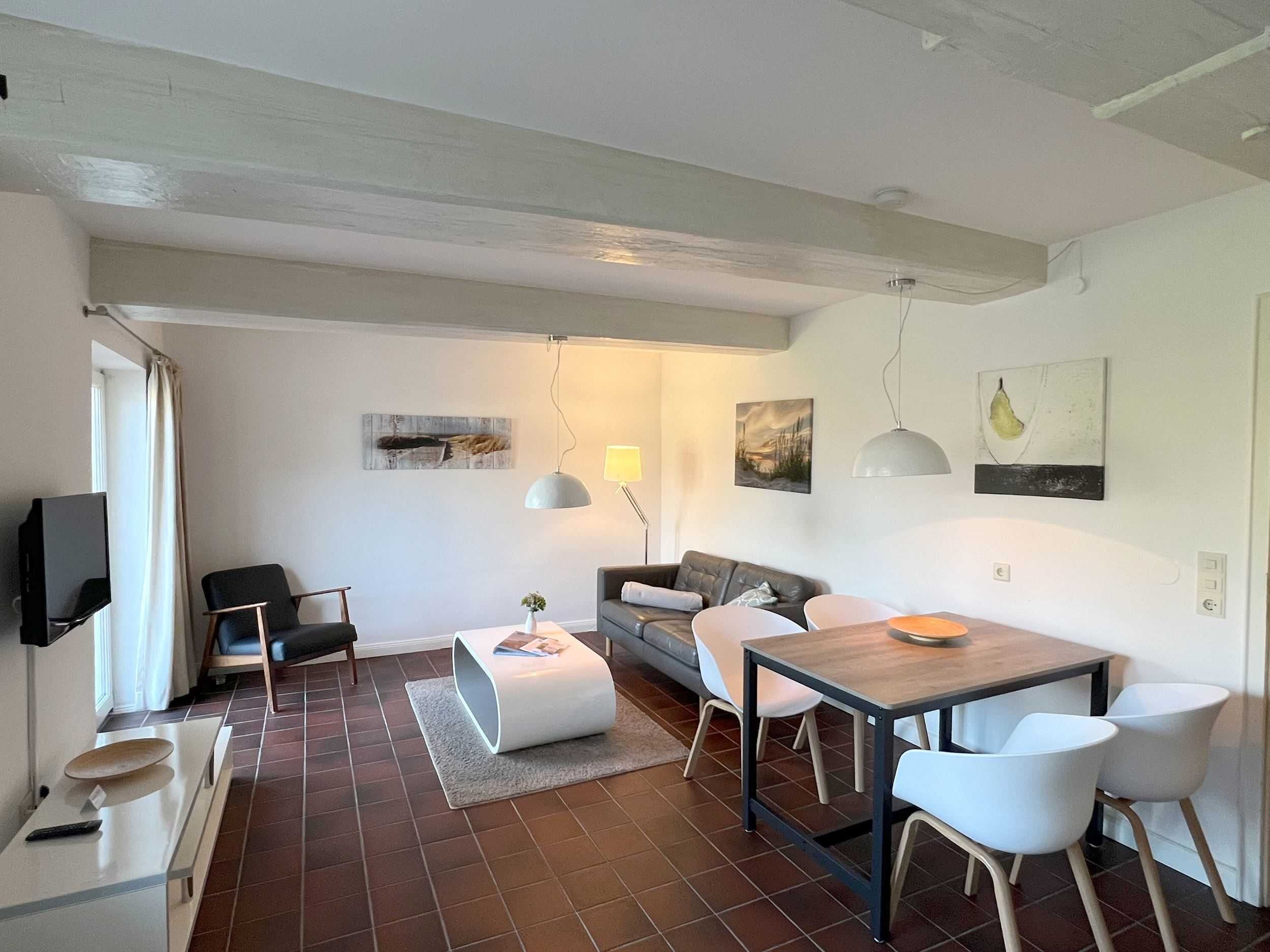 A modern living room with a sofa, a dining table, and chairs. There is a television on the left and artwork on the walls.
