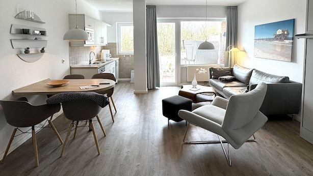 A modern kitchen with a dining area, a sofa, and a view of the outdoors. - Luna IV - Luna Apartment 30 (Sankt Peter-Ording)