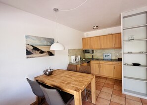 Uma cozinha compacta com armários de madeira, uma mesa de jantar com cadeiras, um lustre e um quadro na parede.